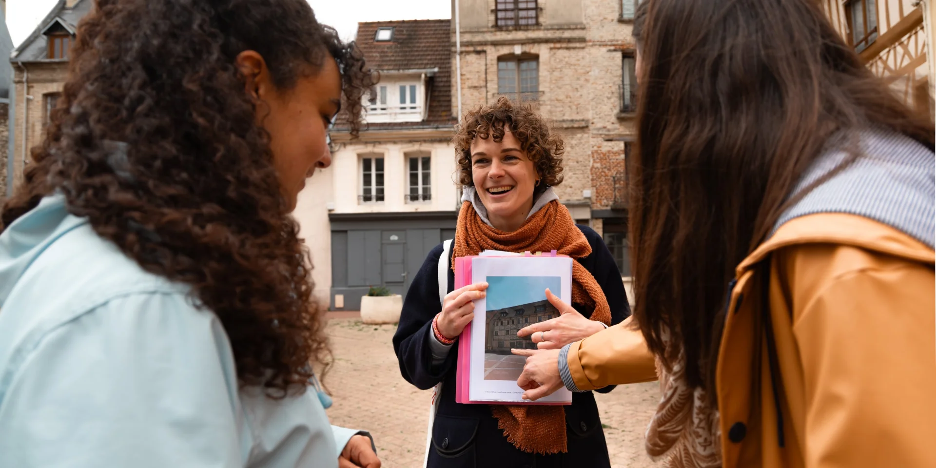 Une guide souriante montre une photo d’archive à deux participantes lors d’une visite commentée dans le centre historique de Dieppe.