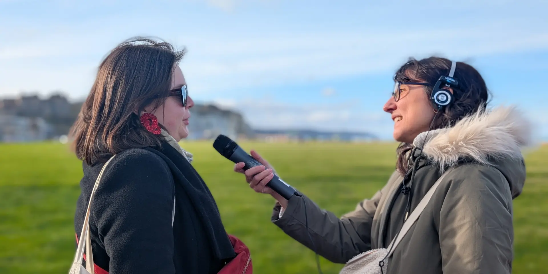 Une journaliste avec un casque et un micro interviewe une jeune femme sur les pelouses de la plage de Dieppe