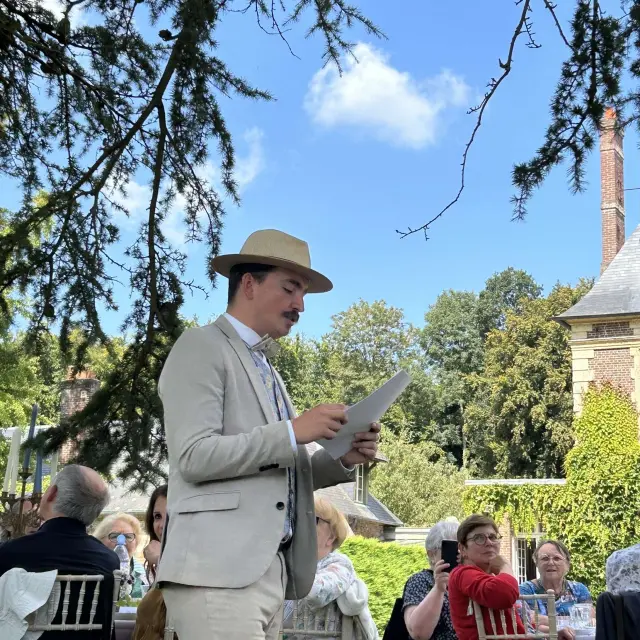 Animateur en tenue d’époque lisant un texte devant un groupe installé dans le parc du château de Miromesnil
