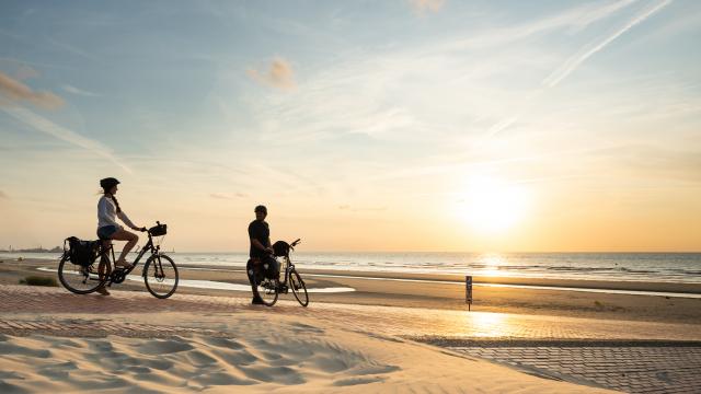 Cyclistes regardant le coucher de soleil sur la plage de Leffrinckoucke