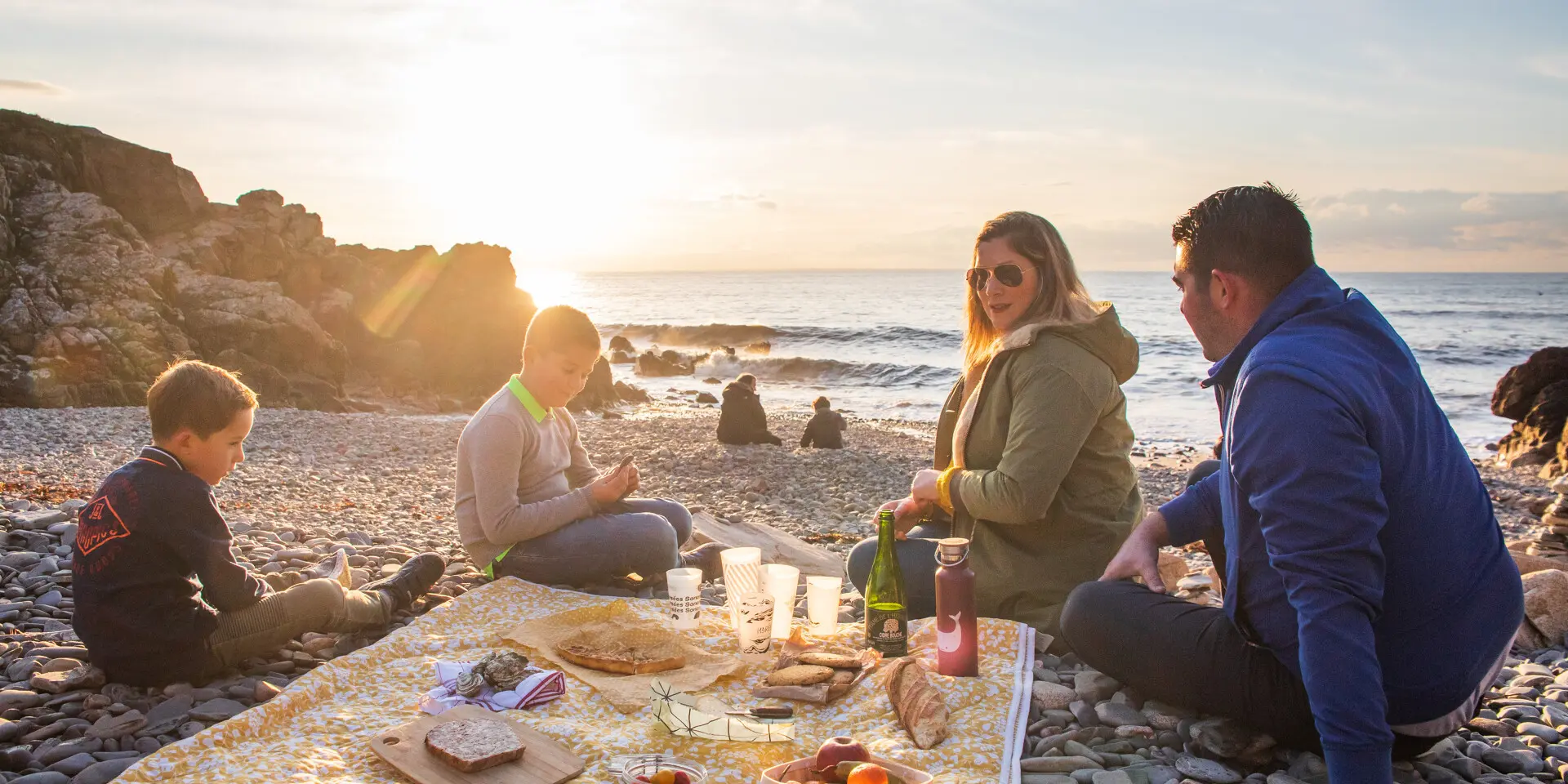 Une famille pique-nique sur les galets du port du Lude au coucher du soleil