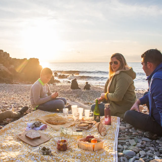 Eine Familie picknickt bei Sonnenuntergang auf den Kieselsteinen des Hafens von Le Lude.