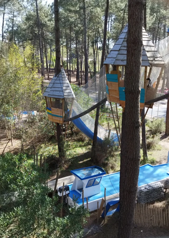 Photo de 2 petites cabanes dans les arbres reliées par un pont de singe entouré d'un filet dans le parc la cité perchée