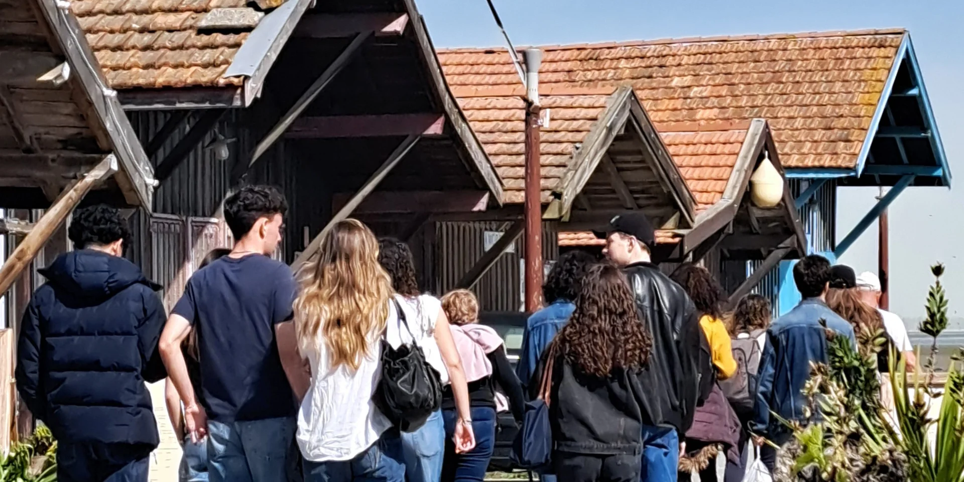 Groupe de personnes qui suit la visite du Port de Larros en passant devant les cabanes ostréicoles