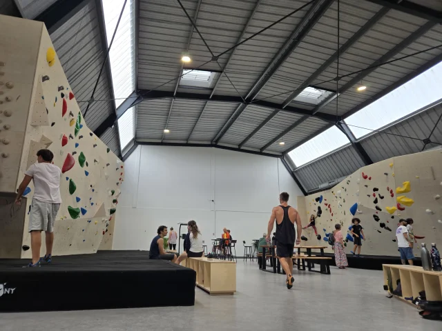 Salle d'escalade avec deux murs grimpes et des personnes se préparant à monter.