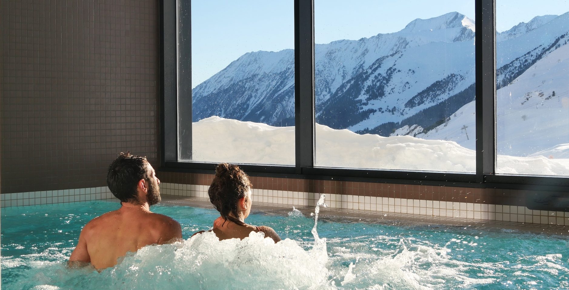 Couple dans un jacuzzi du centre de balnéo Édénéo face aux montagnes enneigées