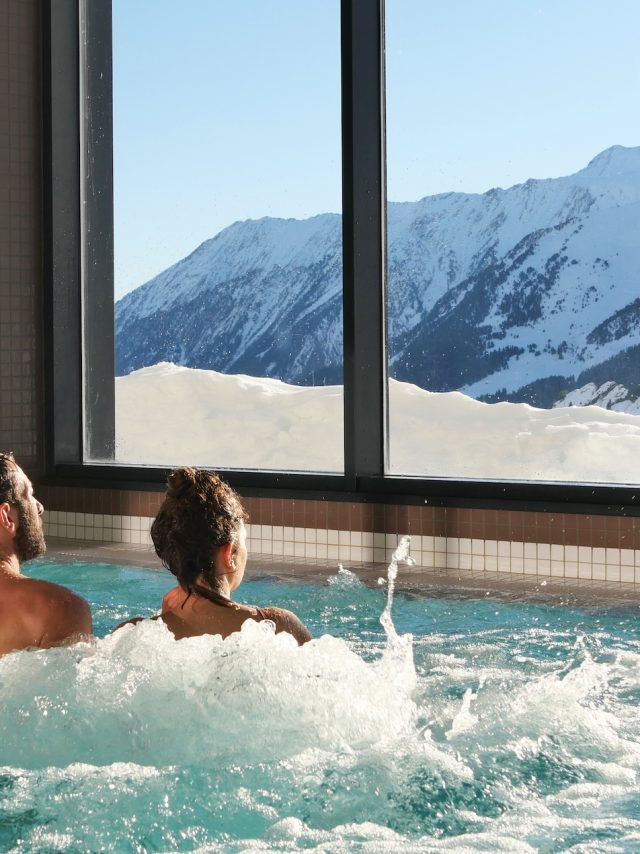 Pareja en un jacuzzi del centro de balneoterapia Édénéo con vistas a las montañas nevadas.
