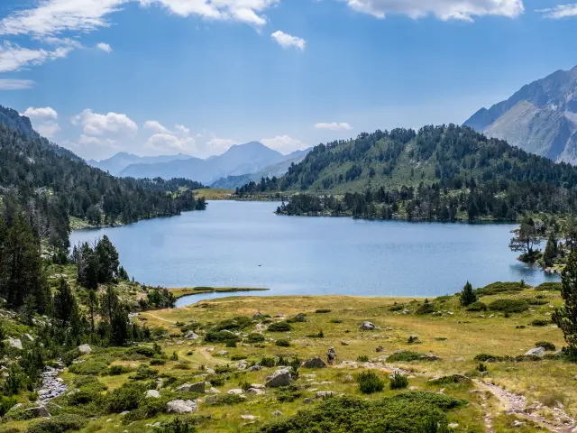 Une randonneuse marche sur un sentier avec le lac d Aumar en arriere plan.