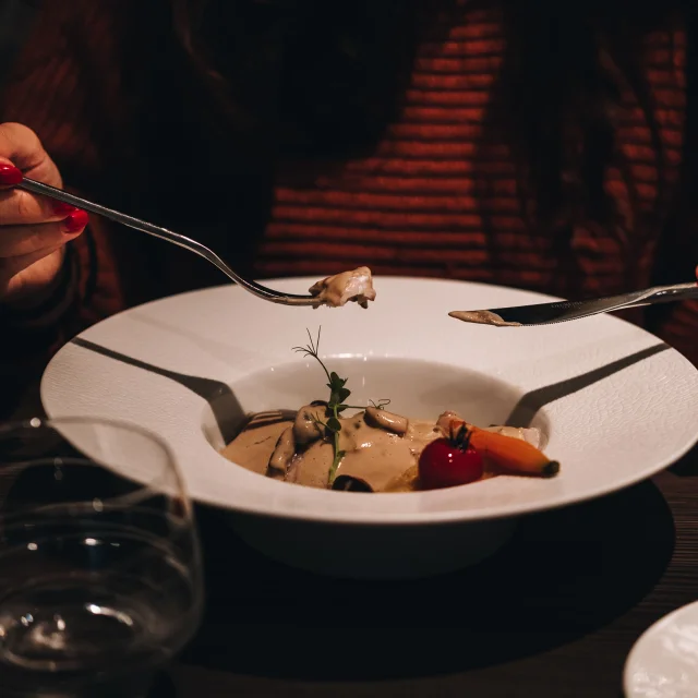 Une femme goûte un plat en sauce servi dans une grande assiette creuse - Vosges du Sud