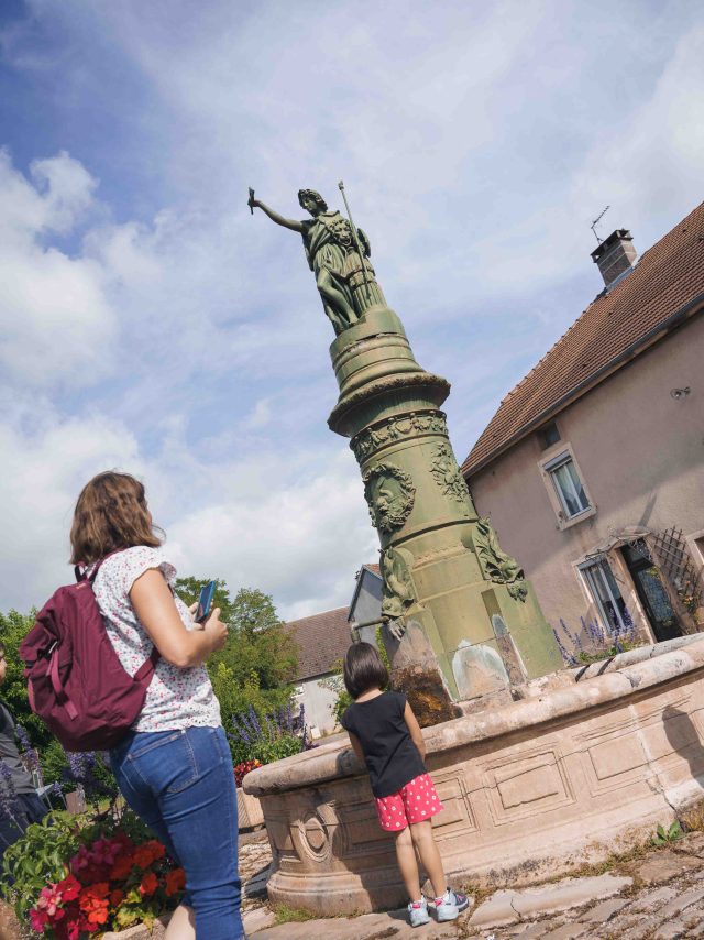 Une famille visite Jussey, grâce à l'application Baludik - On aperçoit une fontaine avec une statue de femme - Vesoul - Val de Saône