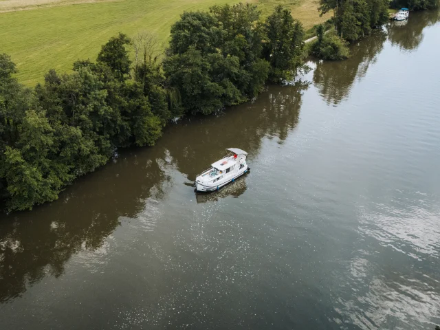 Vue aérienne d'un bateau sans permis navigant sur la Saône, dans un cadre de nature préservée, au milieu de la verdure - Vesoul-Val de Saône