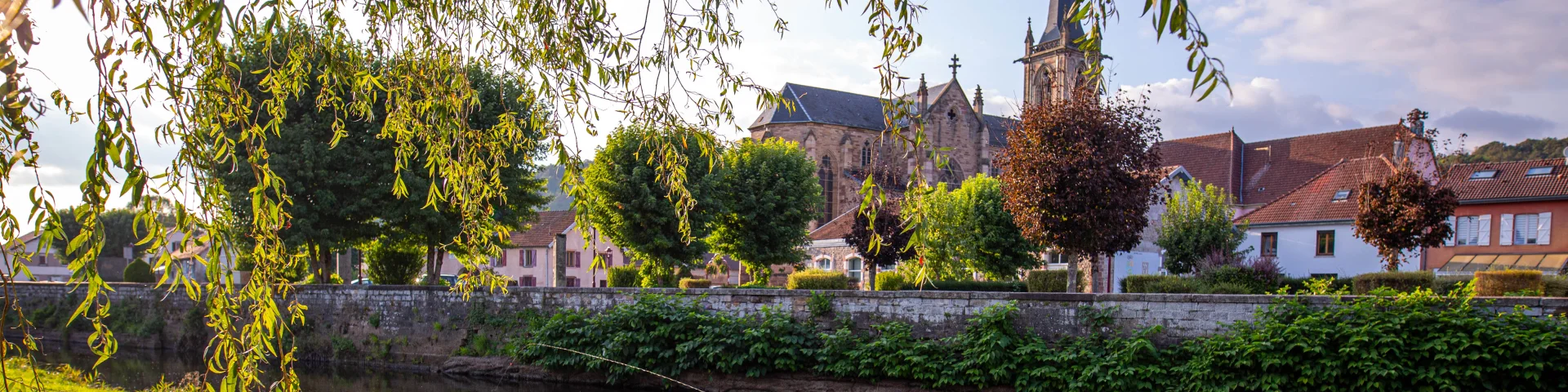 Un homme pêche dans le Rahin à Ronchamp. À l'arrière-plan, on observe la commune avec son église Notre-Dame du Bas - Vosges du Sud
