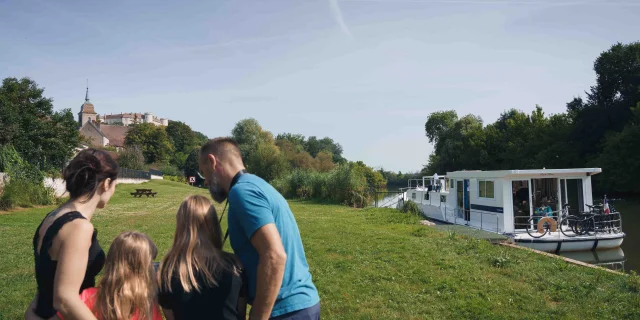 Une famille est en bord de Saône, on aperçoit un bateau de plaisance, en arrière-plan il y a le château de Ray-sur-Saône - Vesoul - Val de Saône