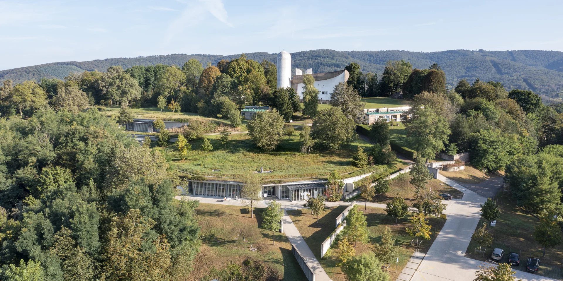 Vue aérienne de la Colline Notre-Dame du Haut, où l'on peut voir La Chapelle Le Corbusier, l'abri du pèlerin, la maison du chapelain. La Porterie et le monastère Sainte-Claire de Renzo Piano sont également visibles - Vosges du Sud