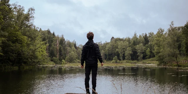 Un homme, debout sur un ponton, observe un étang entouré de forêt sur le Plateau des 1000 Étangs - Vosges du Sud