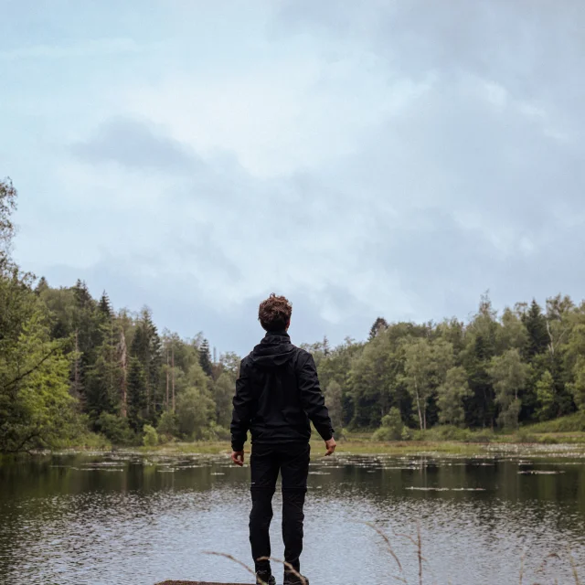 Un homme, debout sur un ponton, observe un étang entouré de forêt sur le Plateau des 1000 Étangs - Vosges du Sud