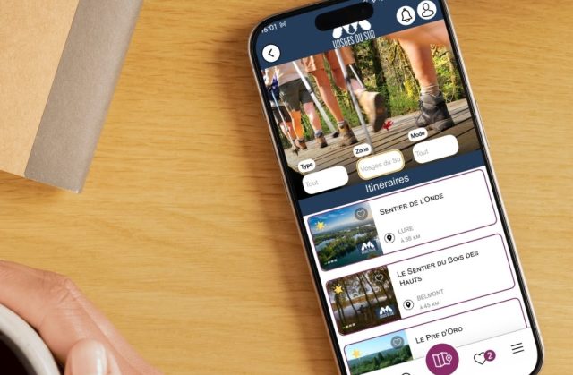 Une personne tient un smartphone avec l'application My Haute-Saône ouverte, permettant de voir les circuits de randonnée à proximité dans la rubrique Itinéraires - Haute-Saône