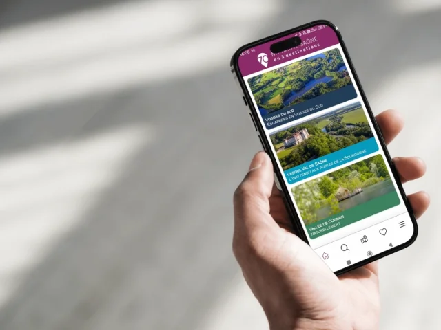 Une personne tient un smartphone avec l'application My Haute-Saône ouverte sur la page d’accueil, présentant les 3 destinations : Vesoul-Val de Saône, Vosges du Sud et Vallée de l’Ognon - Haute-Saône