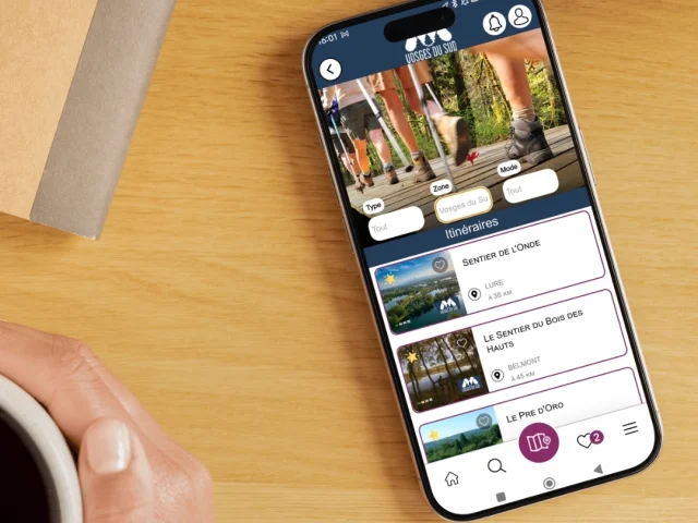 Une personne tient un smartphone avec l'application My Haute-Saône ouverte, permettant de voir les circuits de randonnée à proximité dans la rubrique Itinéraires - Haute-Saône