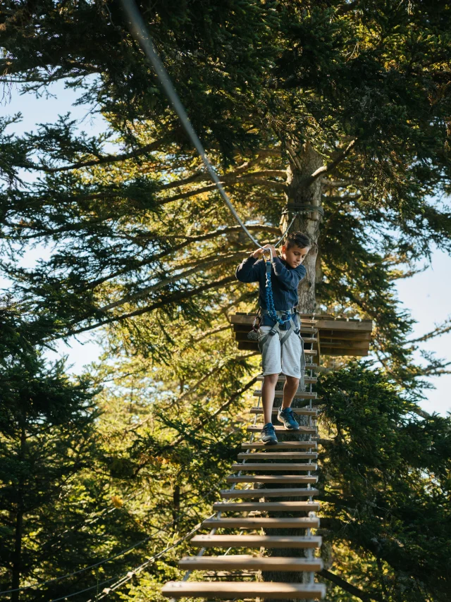 Jeune garçon sur une échelle du parcours aventure