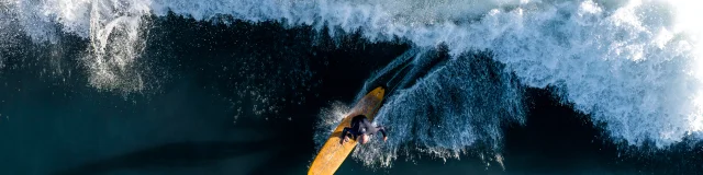 Surfeur capturé en action sur une grande vague vue de haut.