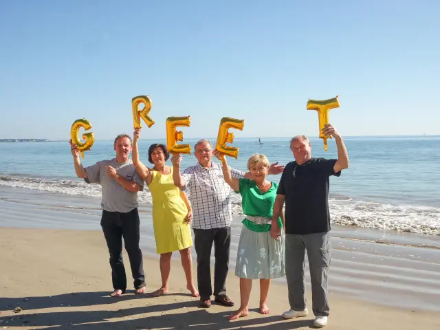 Groupe de greeters sur la plage portant des lettres GREET