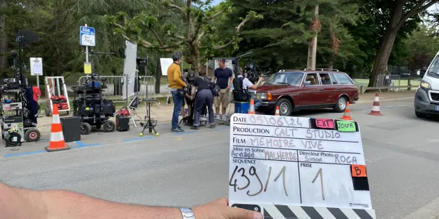 Scène d'un tournage de film avec en 1er plan une main tenant un clap de tournage