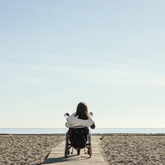 Vue arriere d'une femme en fauteuil roulant à la plage