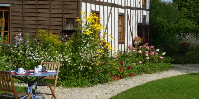Vue sur un jardin et une maison à pans de bois, une petite table de jardin est dressée avec des tasses posées dessus