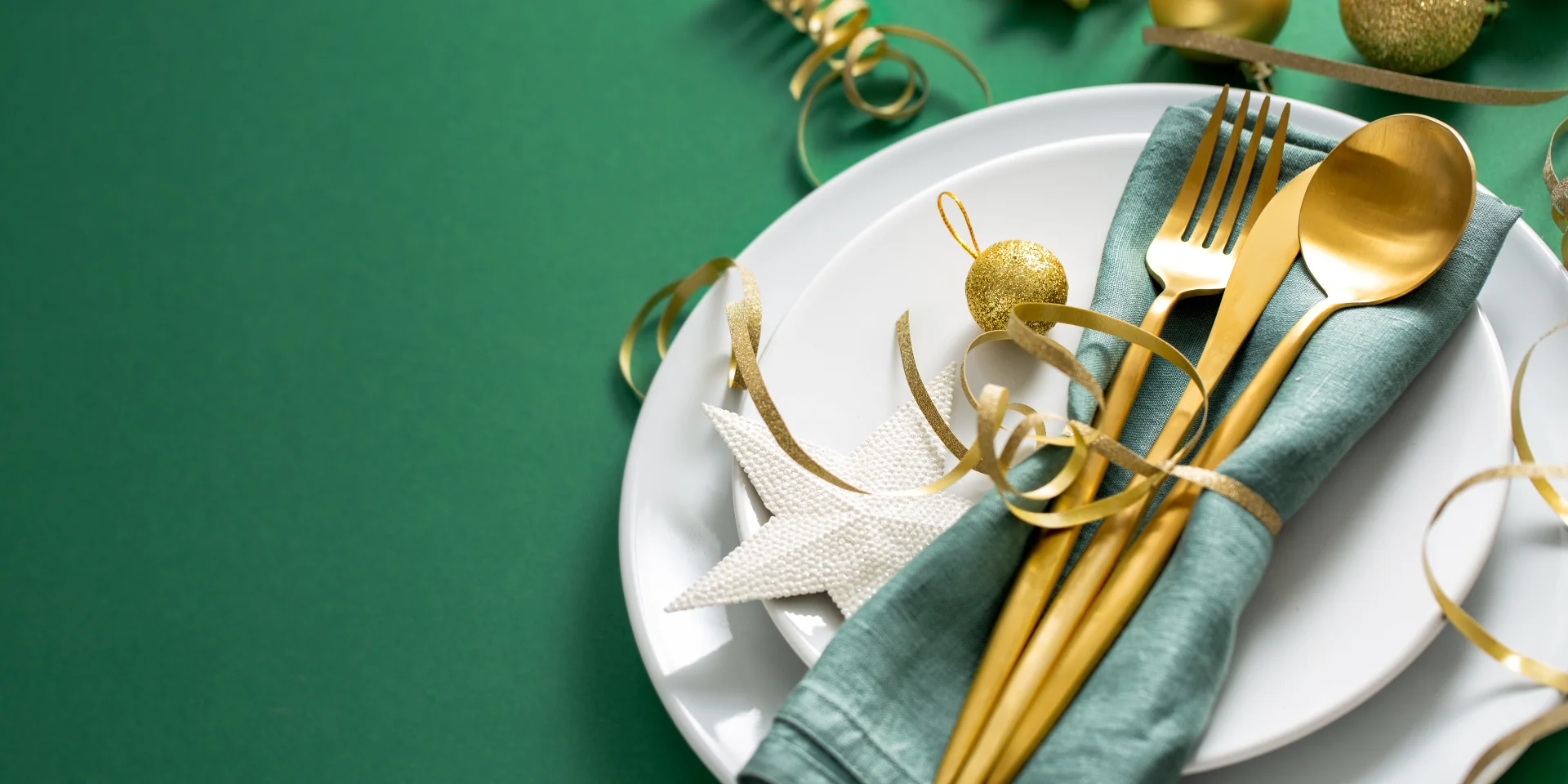 Christmas Flat Lay Background. Gold Cutlery with Bubbles served on napkin on plate on Green Background. Minimalistic design. Copy Space. Horizontal. Christmas concept.