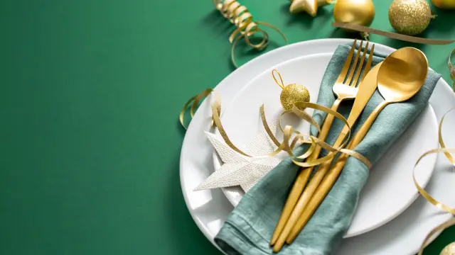 Christmas Flat Lay Background. Gold Cutlery with Bubbles served on napkin on plate on Green Background. Minimalistic design. Copy Space. Horizontal. Christmas concept.