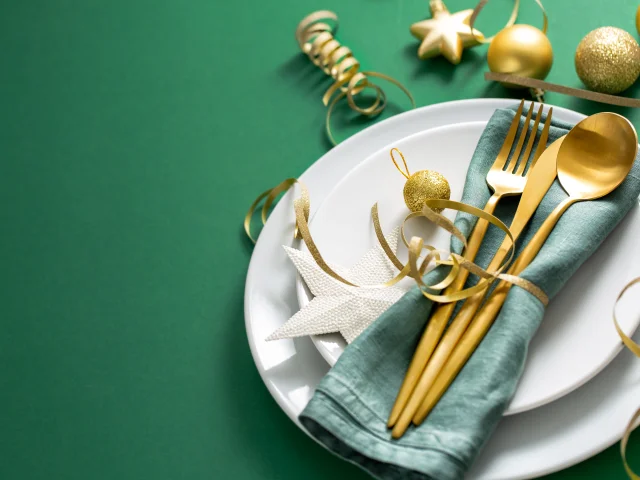 Christmas Flat Lay Background. Gold Cutlery with Bubbles served on napkin on plate on Green Background. Minimalistic design. Copy Space. Horizontal. Christmas concept.