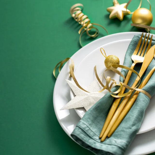 Christmas Flat Lay Background. Gold Cutlery with Bubbles served on napkin on plate on Green Background. Minimalistic design. Copy Space. Horizontal. Christmas concept.