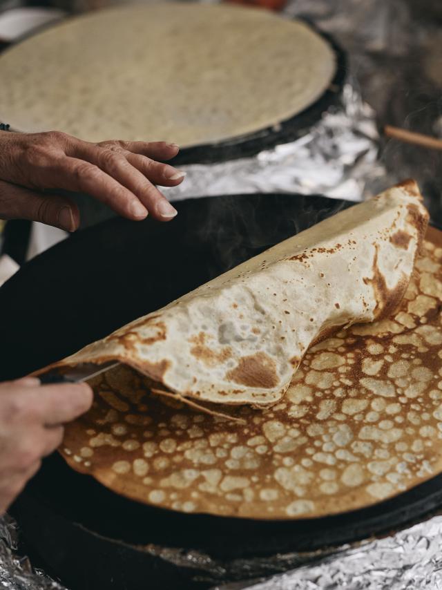 Une femme retourne une crêpe bretonne cuite sur une billig
