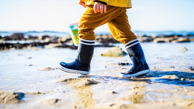 Un enfant marche sur la plage. Il porte des bottes de marin bleues et un cirée jaune