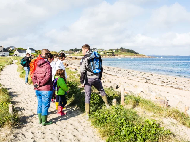 Un groupe de personnes écoute les informations données par un guide le long d'une plage.