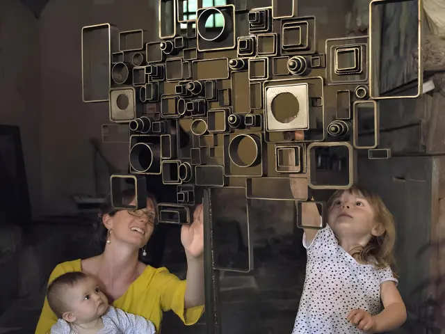 Un femme avec 2 enfants observe un sculpture en métal dans l'enceinte d'une chapelle.