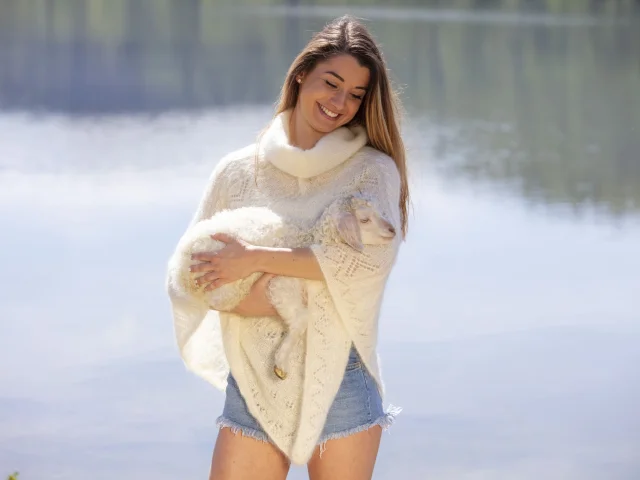 poncho de chez Mohair breizh. La mannequin porte un chèvre angora dans ses bras