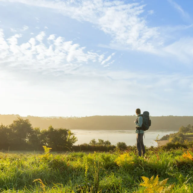 Un randonneur avec un sac à dos sur le GR34 regarde vers la mer.