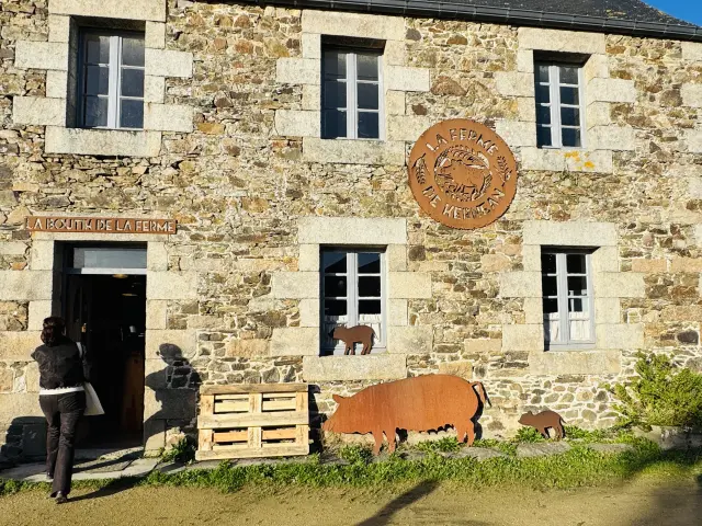 Façade de la boutique de la ferme de Kernéan avec l'entrée et des décorations de porcs en metal posées sur le mur