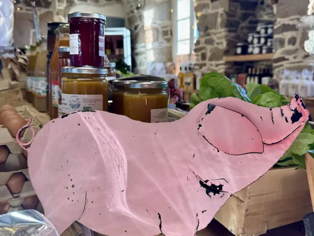 Petit cochon rose en metal posé à côté des produits de la boutique sur une table
