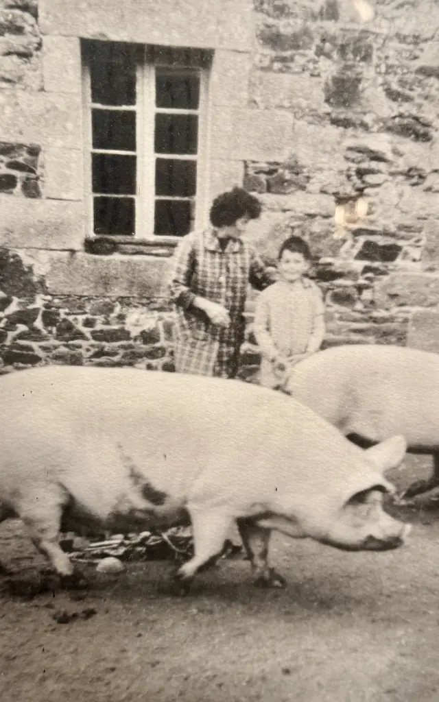 Photo des parents d'Antoine Person devant une maison en pierre et entourés de deux porcs
