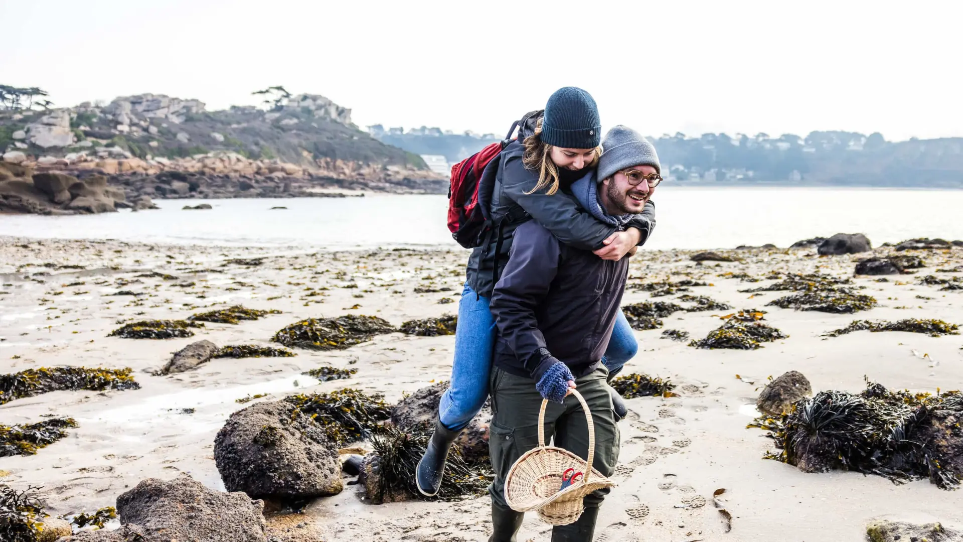 C'est l'hiver ou l'automne, un couple se teint se balade sur une grève. L'Homme porte la femme à califourchon.