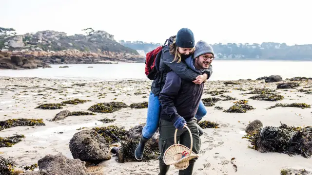 C'est l'hiver ou l'automne, un couple se teint se balade sur une grève. L'Homme porte la femme à califourchon.