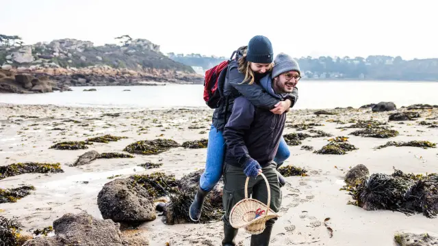 C'est l'hiver ou l'automne, un couple se teint se balade sur une grève. L'Homme porte la femme à califourchon.