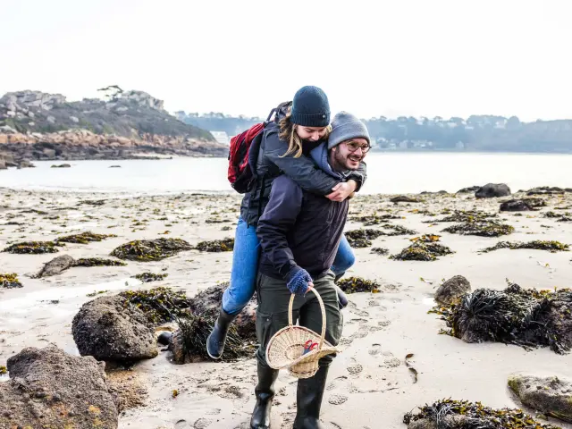 C'est l'hiver ou l'automne, un couple se teint se balade sur une grève. L'Homme porte la femme à califourchon.