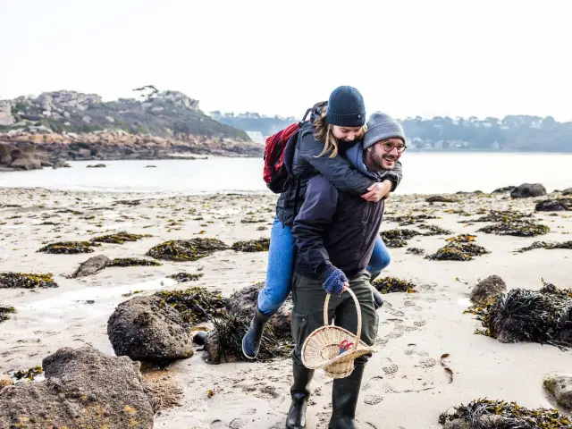 C'est l'hiver ou l'automne, un couple se teint se balade sur une grève. L'Homme porte la femme à califourchon.