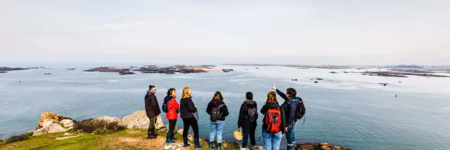 C'est l'hiver ou l'automne, un groupe de personnes regarde le mer du haut d'une falaise et écoute une guide nature