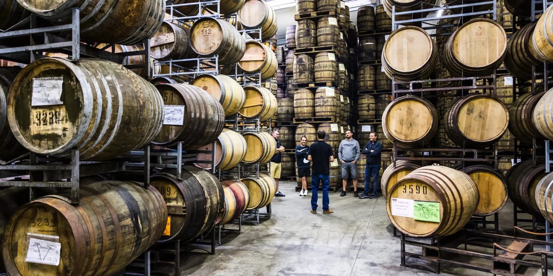 Au milieu de tonneau, un groupe personne visite le chais d'une distillerie de whisky.