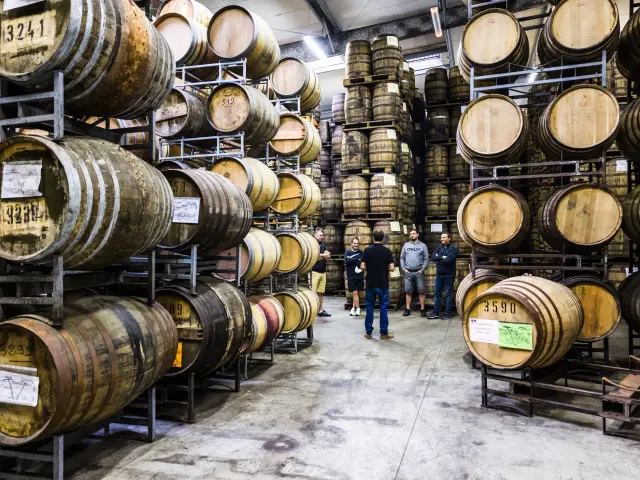 Au milieu de tonneau, un groupe personne visite le chais d'une distillerie de whisky.